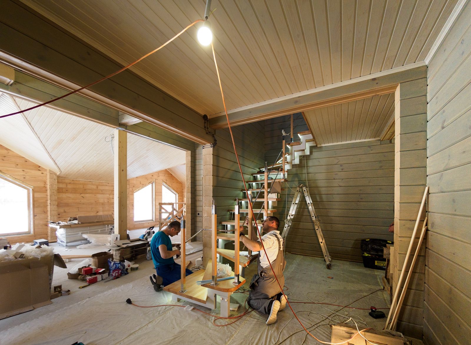 Two installers assembling a wooden staircase inside a home under renovation